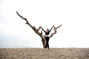 fit sporty woman stretching by a tree on a beach