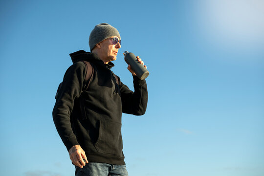 male hiker drinking water from a bottle, outdoors winter sun