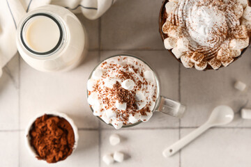 Glass cups of hot cocoa drink with whipped cream and marshmallows on white tile background