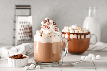 Glass cups of hot cocoa drink with whipped cream and marshmallows on white tile table