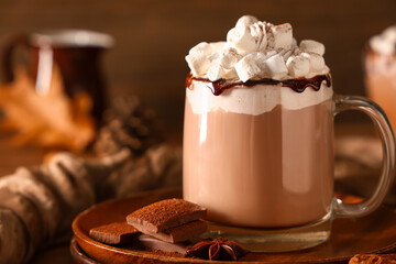 Glass cup of hot cocoa drink with whipped cream and marshmallows on wooden background