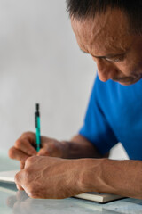 Tight portrait showing man writing with pen, face and left hand visible, four left fingers amputated