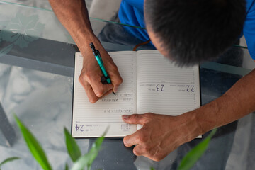 Overhead view of hands filling planner on glass table, clear missing four fingers on left hand, daily planning