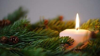 A single lit candle glows warmly amidst the festive greenery of a christmas pine wreath adorned with pinecones creating a serene holiday atmosphere