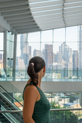 Woman looking at modern city skyline from glass building, symbolizing aspiration, travel, and modern lifestyle concept