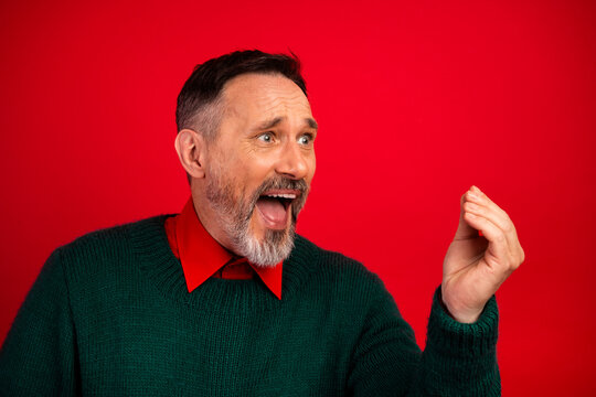 Funny joyful man in green sweater cheers with open mouth and raised hand against bold red background in festive holiday mood for stock photography - Powered by Adobe