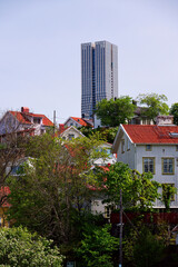 Colony of small wooden historic houses on the Slottsberget mountain with the tallest Scandinavian building Karlatornet skycraper in Lindholmen in background, Gothenburg, Sweden
