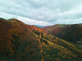 Aerial view of a mountain range in vibrant autumn colors under a cloudy sky. A scenic landscape showcasing the beauty of fall foliage and nature's transition. Beautiful autumn colors.