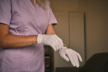 Close-up of a medical professional in scrubs putting on disposable gloves. Depicts hygiene, safety, and clinical preparedness. Suitable for healthcare related themes. 