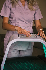 Woman in lilac scrubs operating a light therapy device. Close-up of hands pressing buttons on the machine.  Depicts modern wellness and alternative healthcare practices.
