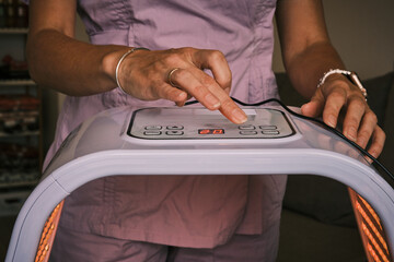 Woman using red light therapy device. Close up on hands adjusting settings on device. Alternative medicine and skin care treatment for health and wellness, at home setting.