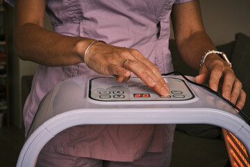 Close-up of hands operating a Low Level LED light therapy device. Ideal for illustrating skincare treatments, phototherapy, or wellness technology. Health and beauty concept in professional spa.