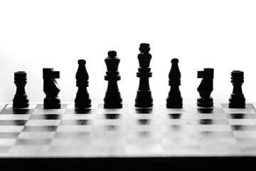 Backlit row of dark wooden chess pieces on a board, minimalist black-and-white silhouette that highlights strategy, hierarchy and focus before the game begins.