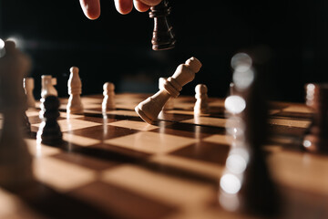 White king tipping over on a wooden chessboard under dramatic light, symbolizing defeat, checkmate,...