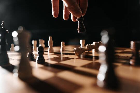 A hand lifts a dark king from the board as a white king lies down; narrative image of reversal, capture and the closing act of play.