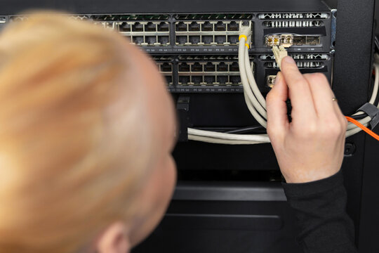 Male IT technician in a data center connecting ethernet cables to a network switch today