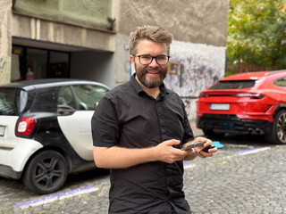 Man using smartphone on city street near parked cars. Technology, urban lifestyle, and everyday communication in modern environment.