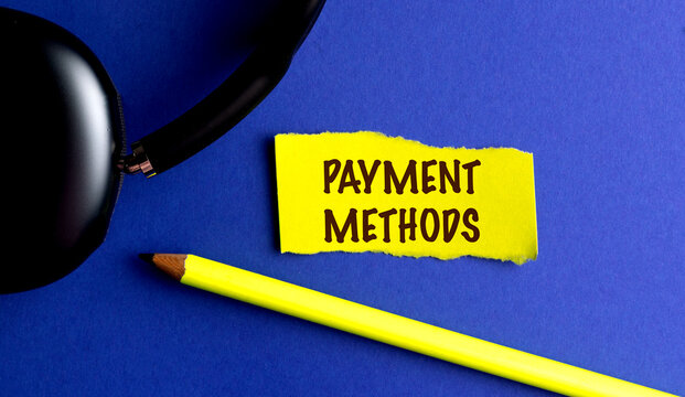 Words payment methods on yellow torn paper with pencil and headphones on blue background