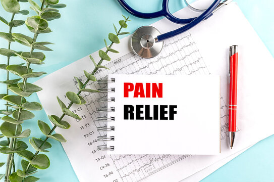 Words pain relief written on notepad with stethoscope, ECG charts and red pen on light blue background