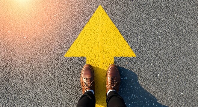 Confident footsteps advance forward on bright yellow arrow painted on asphalt, symbolizing progress and clear direction in life's journey.
