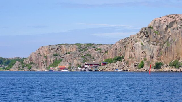Red wooden houses and Bohus granite or swedish Bohusgranit type of granite rocks coastline found along the west coast of Sweden, in Bohusl&auml;n. Slow motion shot from moving boat on sunny summer evening