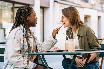 Diverse women friends enjoying brunch feeding each other
