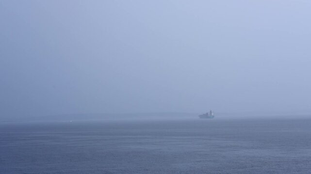 Container ship floating in the middle of a foggy cloud. Cargo ship on sea horizon in mist or rain cloud on the ocean
