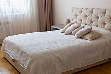 Bedroom interior. Cozy bedroom featuring elegant headboard, soft bedding and decorative pillows, creating serene atmosphere with natural light filtering through sheer curtains enhancing tranquil space