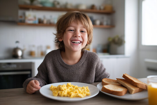 Happy young boy smiling with delight at breakfast, with scrambled eggs and toast on the table. Sunny morning meal for a child. - Powered by Adobe