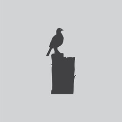 a solitary bird perched atop a dark weathered stone structure against a muted gray backdrop