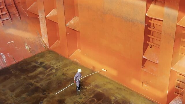 Crew cleaning bulk carrier hold after discharging petroleum coke using seawater, chemicals, and brushes. 4