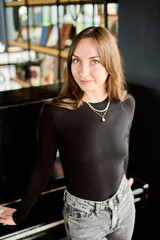 Young woman with light brown hair standing by black piano in cozy room