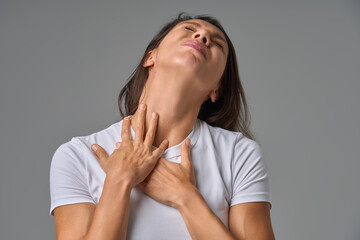 Woman touching chest and neck with eyes closed showing discomfort or sore throat indoors