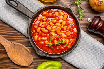Baked bean dish in cast iron pan on wooden background.