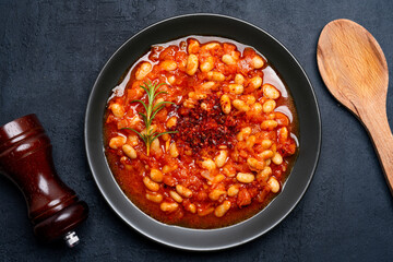 Baked bean dish in  black plate  on black background.