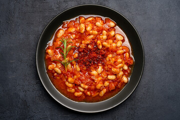 Baked bean dish in  black plate  on black background.