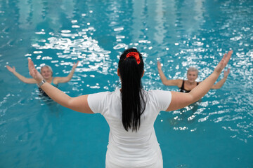 Instructor leading aquatic fitness training for group senior women in a swimming pool. Concept of health, exercise, wellness, water therapy, and active aging lifestyle