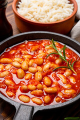 Baked bean dish in cast iron pan on wooden background.