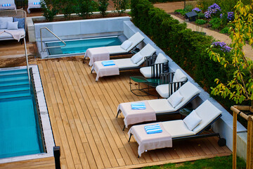Relaxation zone with sun loungers and striped towels on wooden deck and blue pool surrounded by greenery at modern hotel