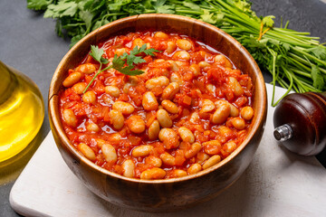 Baked bean dish in wooden bowl on black background. 