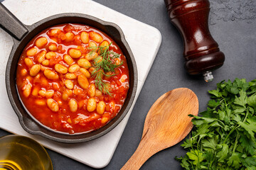 Baked bean dish in cast iron pan on black background. 