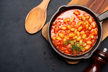Baked bean dish in cast iron pan on black background. 
