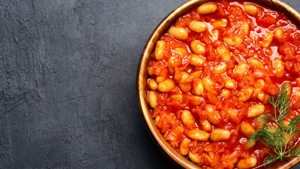 Baked bean dish in wooden bowl on black background. 