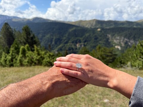 Landscape romantic couple moment in Montenegro with hands together showing an elegant oval diamond engagement ring sparkling in the natural light and scenic background. - Powered by Adobe