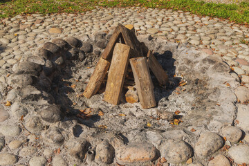 Campfire circle with stones and neatly arranged wooden logs under sunlight. The image evokes outdoor recreation, camping, and rustic lifestyle.