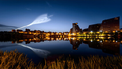 Obraz premium Rocket Launch Over City Skyline at Twilight with Water Reflections
