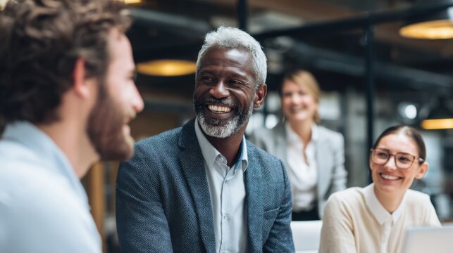 A man with a beard and gray hair is smiling at a group of people. The group consists of a man and a woman, both of whom are smiling. The man is wearing a suit and tie - Powered by Adobe