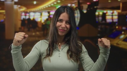 Woman celebrating inside a lively casino with slot machines, exuding joy and excitement, showcasing a winning moment in an indoor gaming environment.