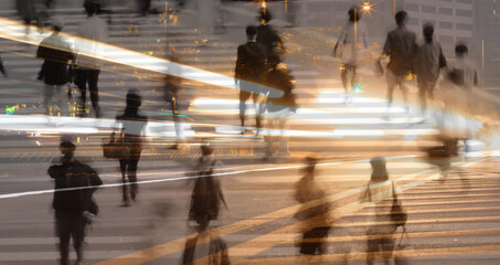 Double exposure of people crossing a busy city street at night with motion lights, symbolizing...