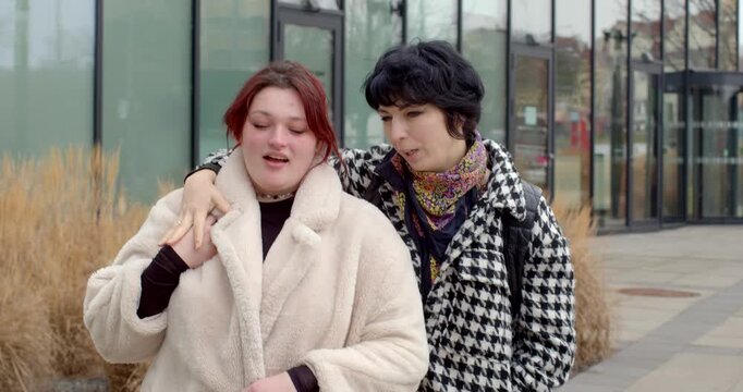 white bride-to-be and asian friend arm-over-shoulder pose on city walkway, playful glances and matching winter looks with faux fur coat and houndstooth jacket, confident bachelorette duo exploring